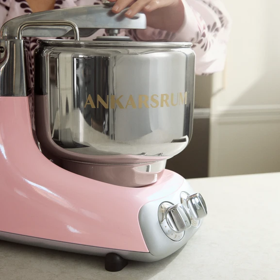 Ankarsrum Assistent Original in de kleur Cloudy Pink, met een persoon op de achtergrond die de machine aanraakt.