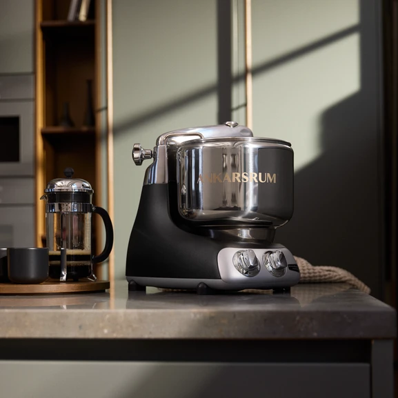 Ankarsrum Assistent Original en noir sur un plan de travail de cuisine en marbre, avec une cafetière à piston noire à côté.