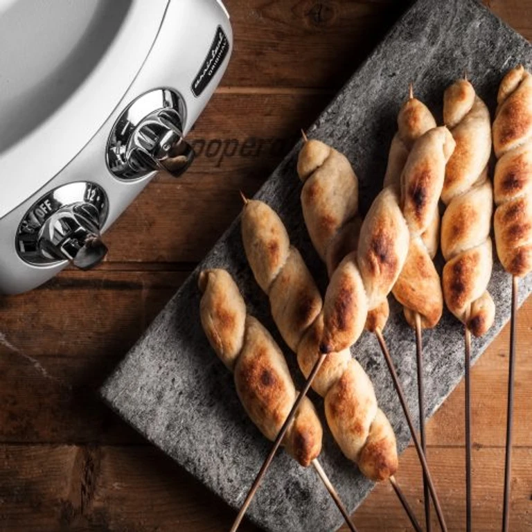 Twisted bread-wrapped sausages on skewers displayed on slate board beside Ankarsrum stand mixer appliance.