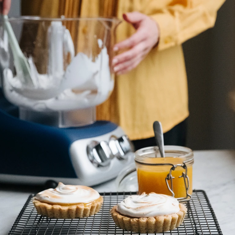 Ankarsrum stand mixer whipping meringue for lemon curd tartlets on a cooling rack in a modern kitchen.