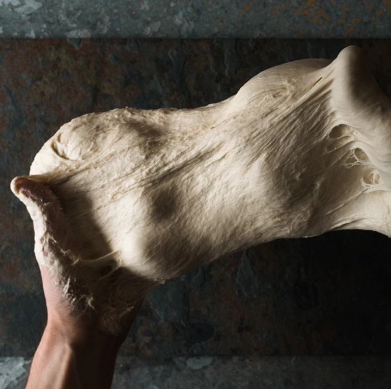 Hands stretching elastic bread dough, showcasing the perfect gluten development achieved with an Ankarsrum stand mixer.