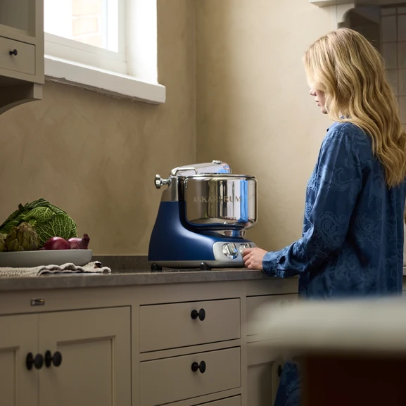 Ankarsrum Assistent Original in Royal Blue in a kitchen, with a woman standing in front of the machine.