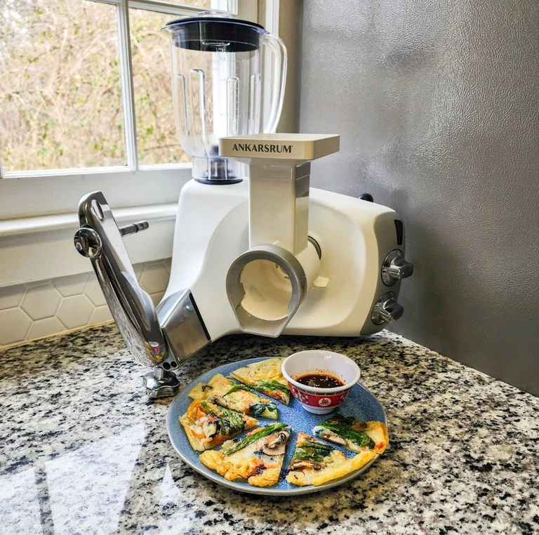Asian crepes filled with fresh vegetables served with spicy dipping sauce with the Ankarsrum stand mixer pictured behind with the slicer/shredder and blender attachments.