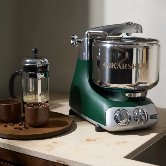 Ankarsrum Assistent Original in Forest Green on a light kitchen countertop, with a French press and coffee beans beside it.