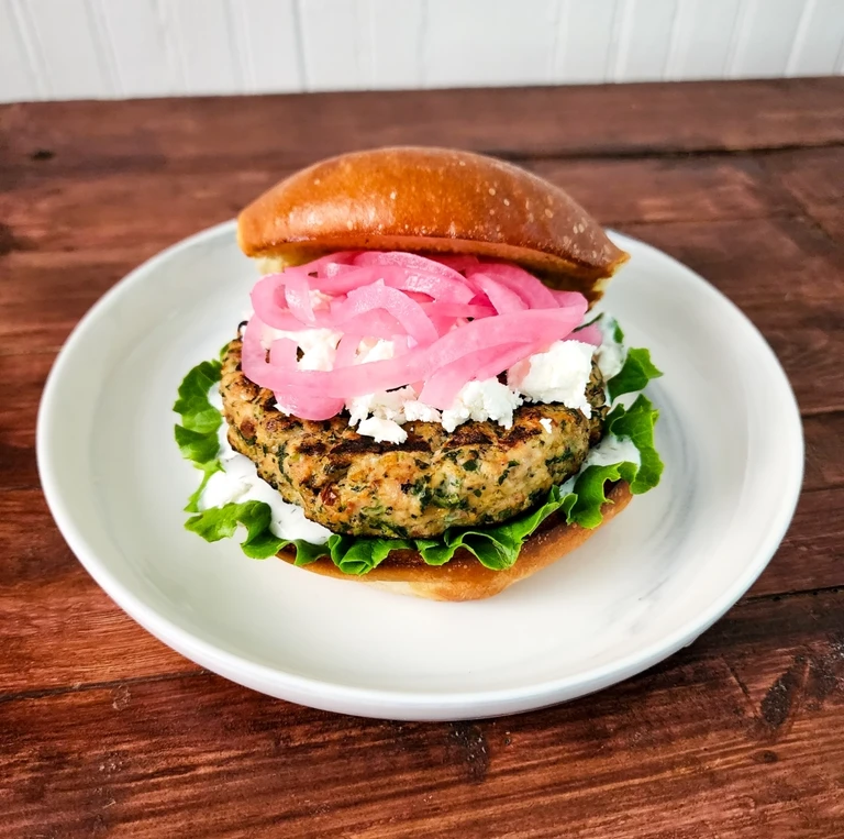 Greek-style chicken burger with feta, pickled red onions, lettuce, and tzatziki on a brioche bun, made with Ankarsrum mixer.