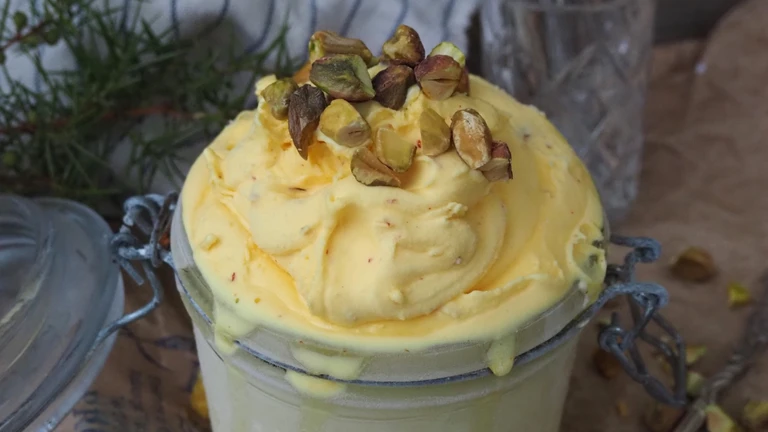 Creamy pistachio ice cream overflowing a glass jar, topped with chopped pistachios, made with an Ankarsrum stand mixer.