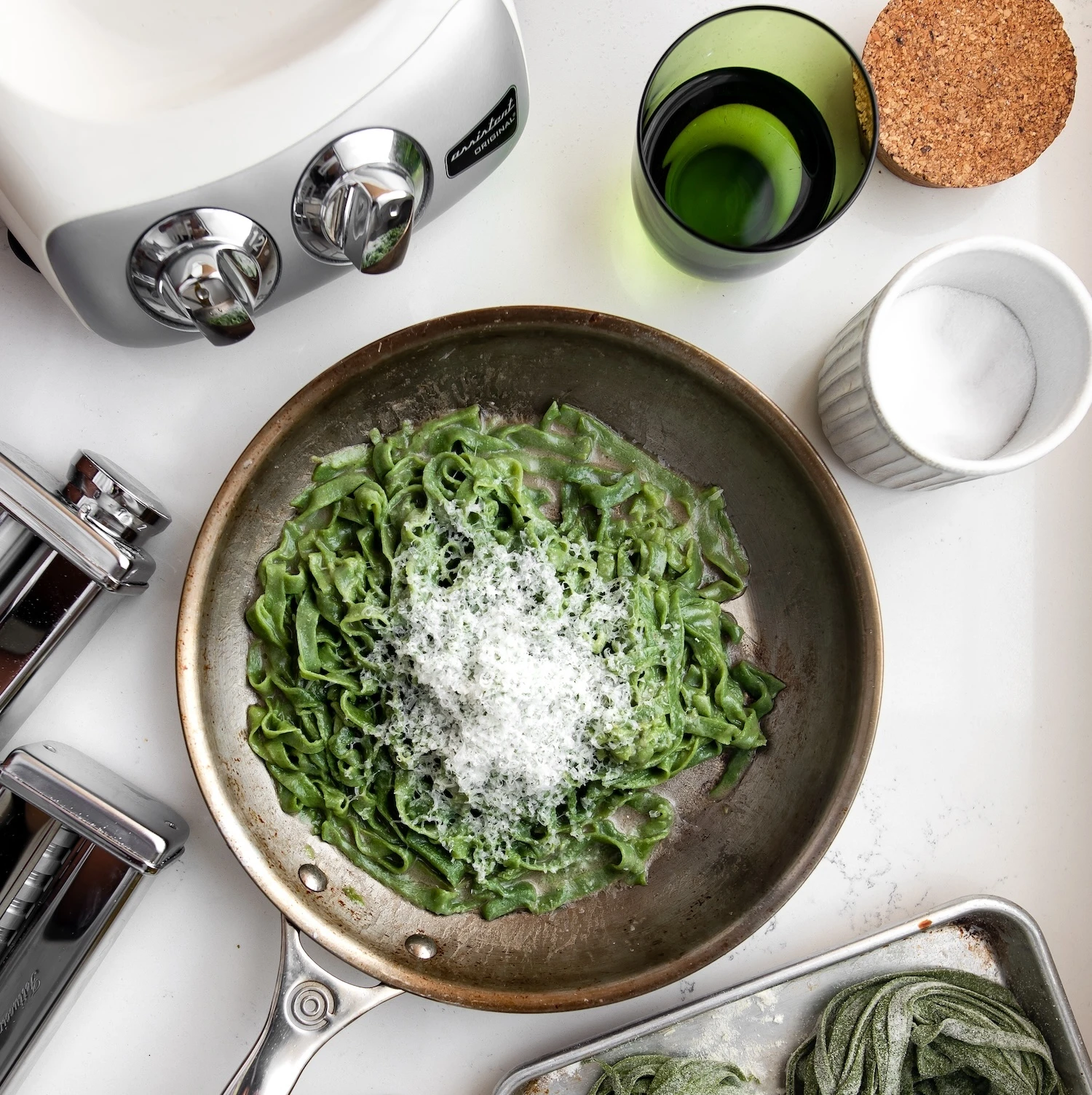 Ankarsrum stand mixer beside fresh green spinach tagliatelle pasta topped with grated parmesan in a skillet pan.