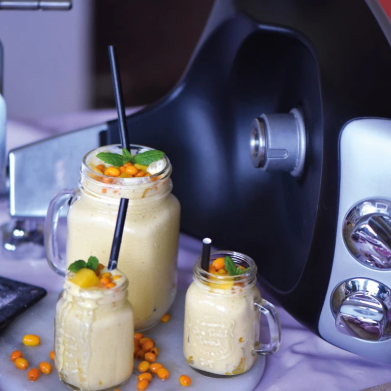 Three creamy sea buckthorn smoothies in mason jar mugs with mint garnish, made with Ankarsrum stand mixer in background.