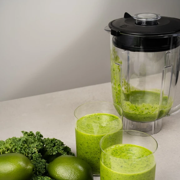Mixer auf einer Küchenarbeitsplatte mit zwei Gläsern grünem Smoothie daneben.