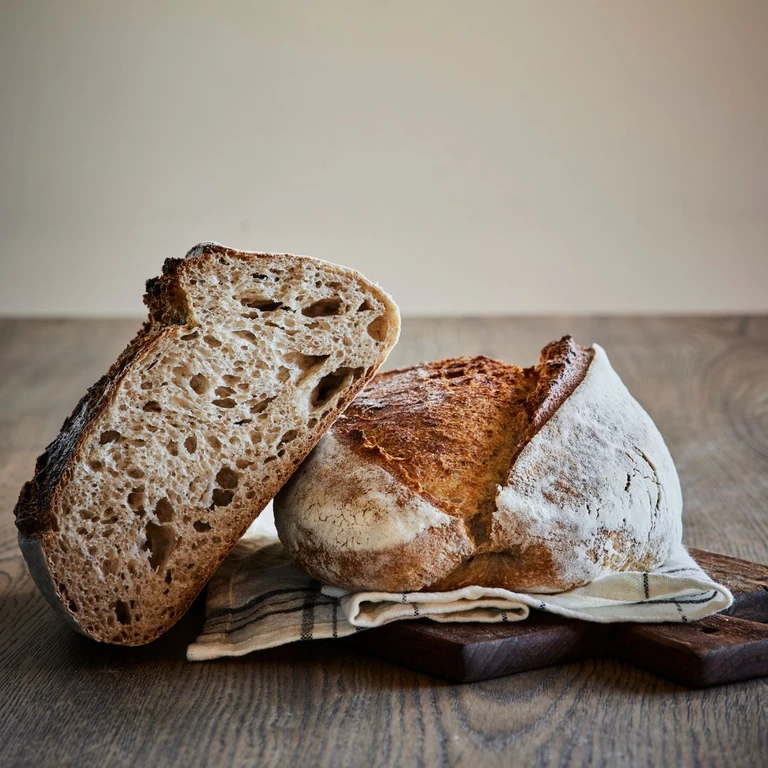 Freshly baked sourdough bread loaf cut open, showing airy open crumb, dusted with flour on a rustic wooden board.