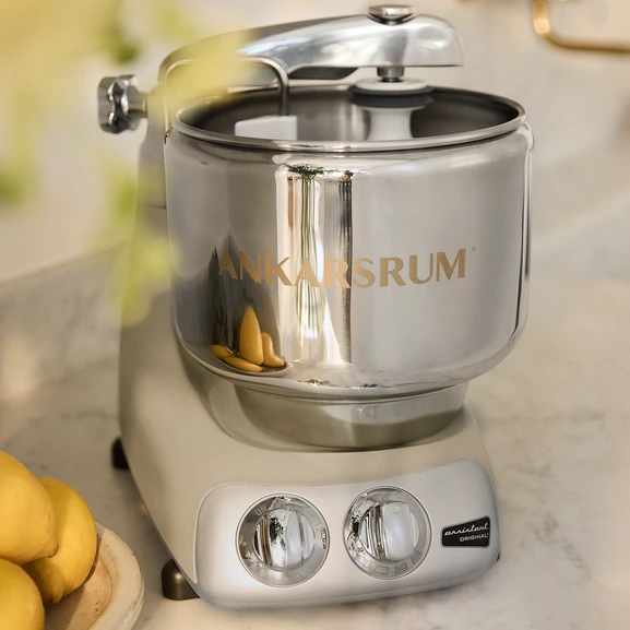 Close-up of the Ankarsrum Assistent Original in Harmony Beige in a bright kitchen, with a few lemons visible beside it.