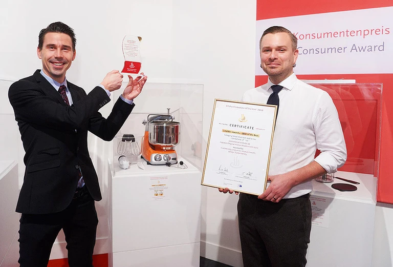 Two men hold a Golden Award – Best of the Best certificate and trophy at the Konsumentenpreis Consumer Award for Ankarsrum.
