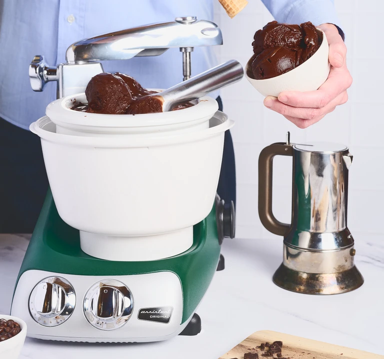 Ankarsrum Original stand mixer in olive green with ice cream maker attachment with chocolate ice cream, served in a white bowl.