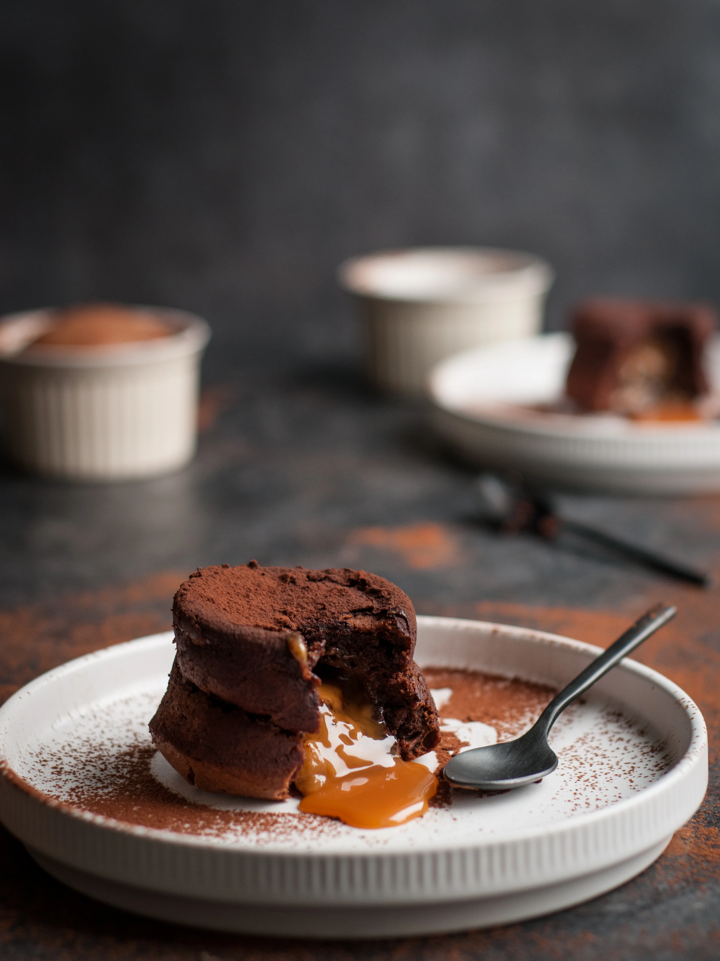 Chocolate lava cake with caramel filling oozing onto a white plate, dusted with cocoa powder, spoon alongside.