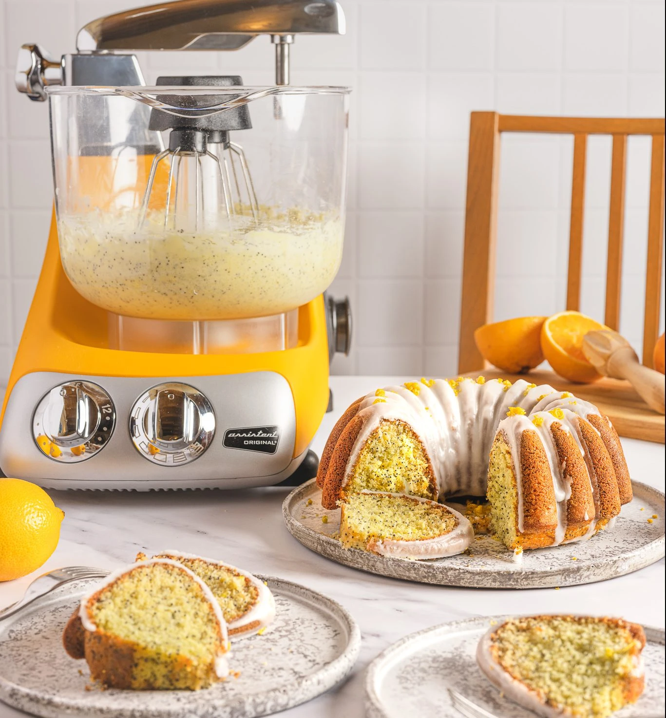 Ankarsrum Assistent Original sunbeam yellow stand mixer with lemon poppy seed bundt cake batter, beside a glazed finished cake.