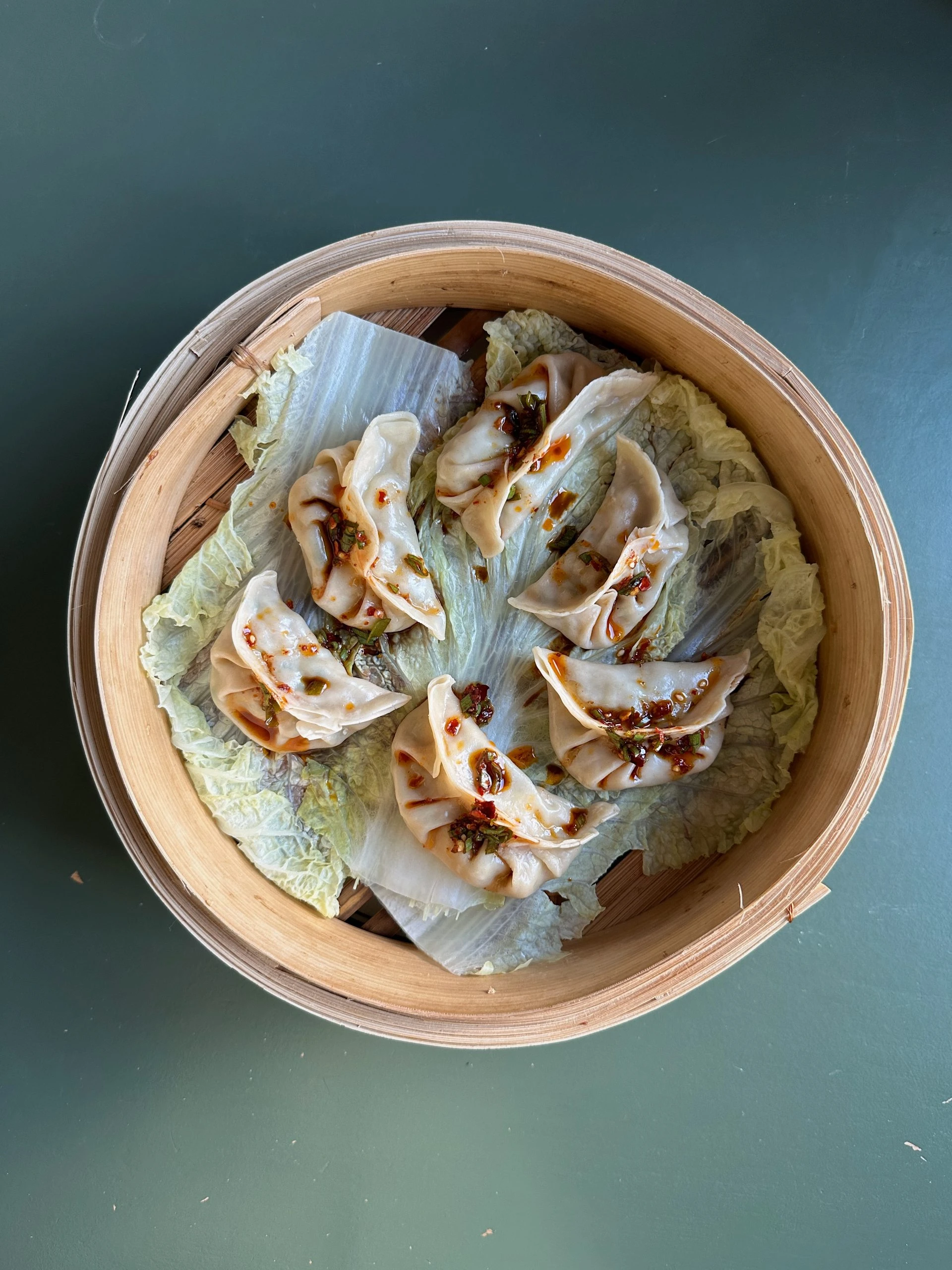 Steamed dumplings with chili sauce on napa cabbage in a bamboo steamer, made with Ankarsrum stand mixer pasta attachment.