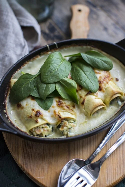 Baked cannelloni filled with spinach and ricotta in creamy béchamel sauce, served in a cast iron skillet.