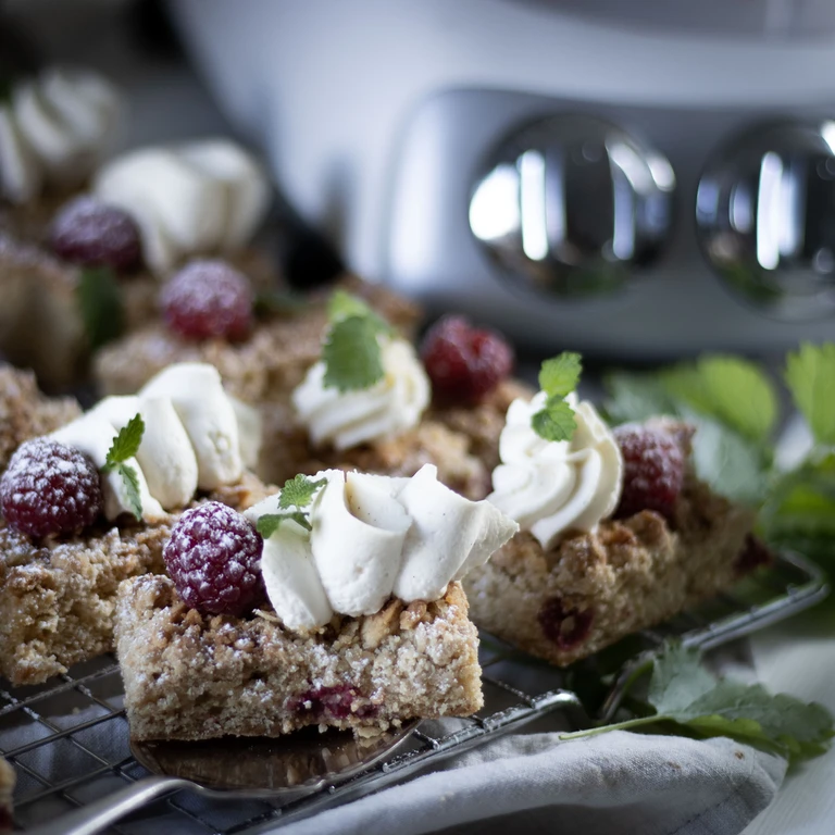 Raspberry crumble bars topped with whipped cream and fresh mint on a cooling rack, made with an Ankarsrum stand mixer.