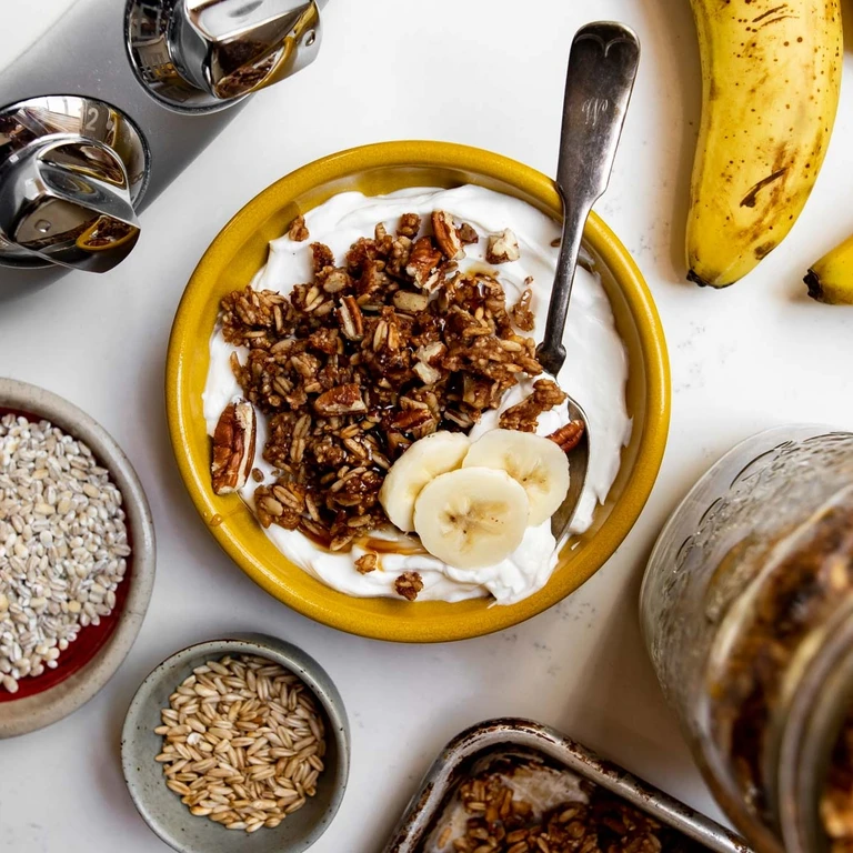 Yogurt bowl topped with homemade banana-bread granola, topped with banana slices and pecans.