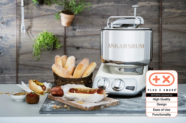 Ankarsrum Original stand mixer in chrome beside homemade hot dog buns and sausages; Plus X Award 2017/2018 winner.