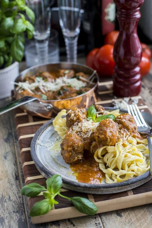Homemade meatballs in rich tomato sauce over fettuccine pasta, topped with grated Parmesan and fresh basil leaves.