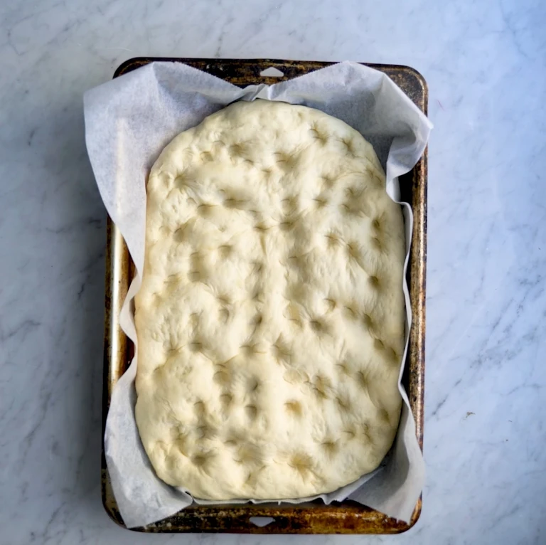 Unbaked focaccia dough with dimples on parchment-lined baking tray, ready for the oven, made with Ankarsrum stand mixer.