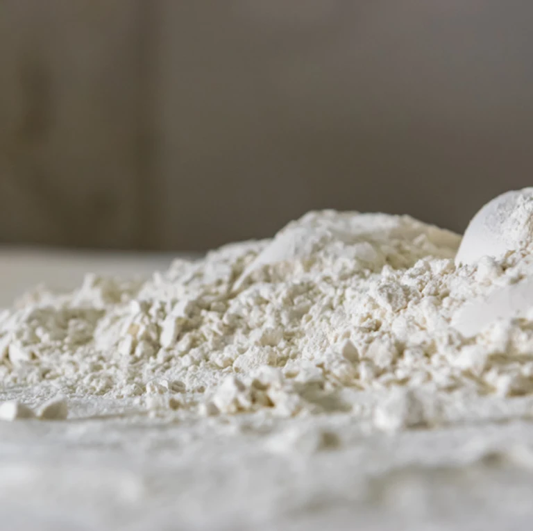 Close-up of fine white flour spilled on a surface with a measuring scoop, ideal for use with Ankarsrum stand mixers.