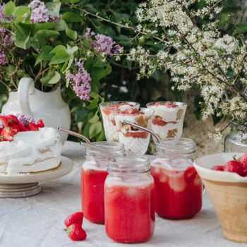 Midsommartårta dekorerad med färska jordgubbar och blommor, serverad på ett vitt bord i en solig trädgård.