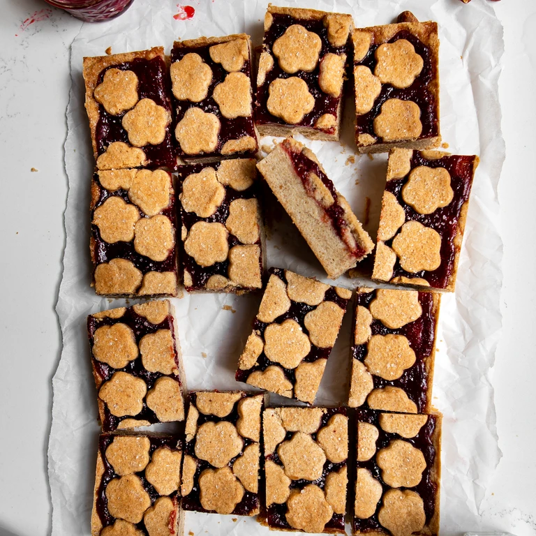 Freshly baked jam bars with flower-shaped shortbread cookie toppings and glossy berry jam filling, cut into squares.