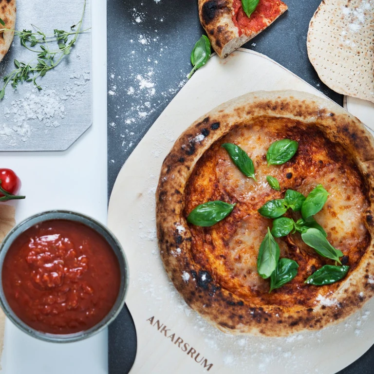 Freshly baked Neapolitan pizza with basil on an Ankarsrum pizza stone, served with tomato sauce.