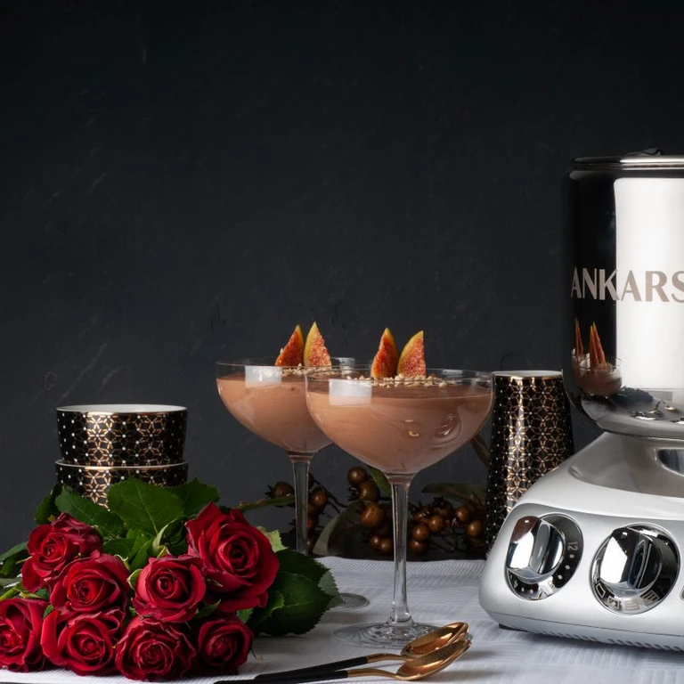 Two chocolate mousse desserts in coupe glasses garnished with figs, beside an Ankarsrum stand mixer and red roses.