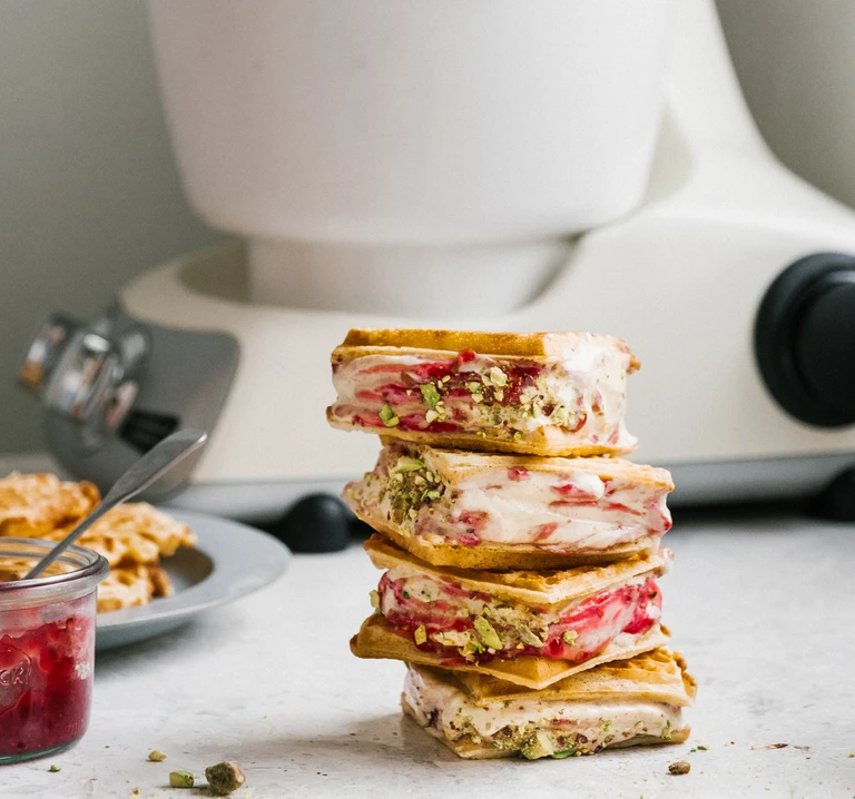 Stacked waffle ice cream sandwiches with raspberry swirl and pistachios, made with Ankarsrum stand mixer in background.
