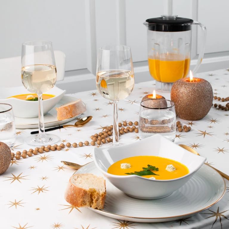 Ankarsrum blender filled with pumpkin soup beside elegant holiday table setting with bowls, wine glasses, and candles.