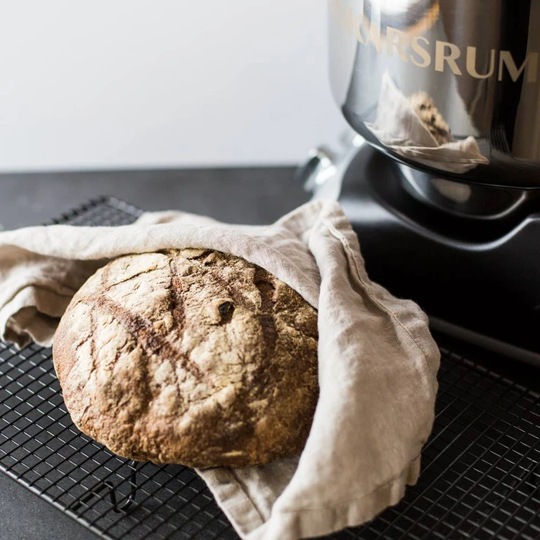 Freshly baked rustic sourdough bread on a cooling rack beside an Ankarsrum stand mixer in black.