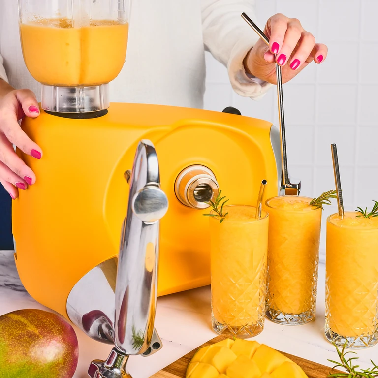 Ankarsrum sunbeam yellow stand mixer blending mango smoothies into crystal glasses with metal straws and rosemary garnish.