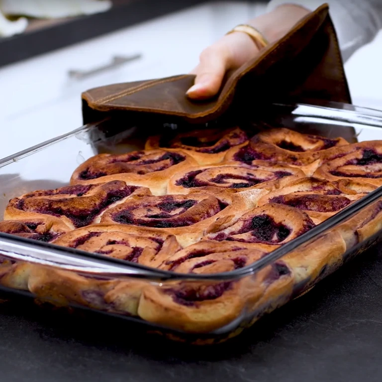 Freshly baked blueberry sweet rolls in a glass baking dish, held with a leather oven mitt.