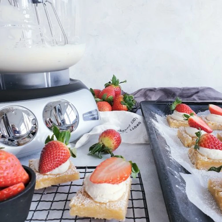 Ankarsrum stand mixer with cream beside strawberry shortcake bars dusted with powdered sugar on a cooling rack.