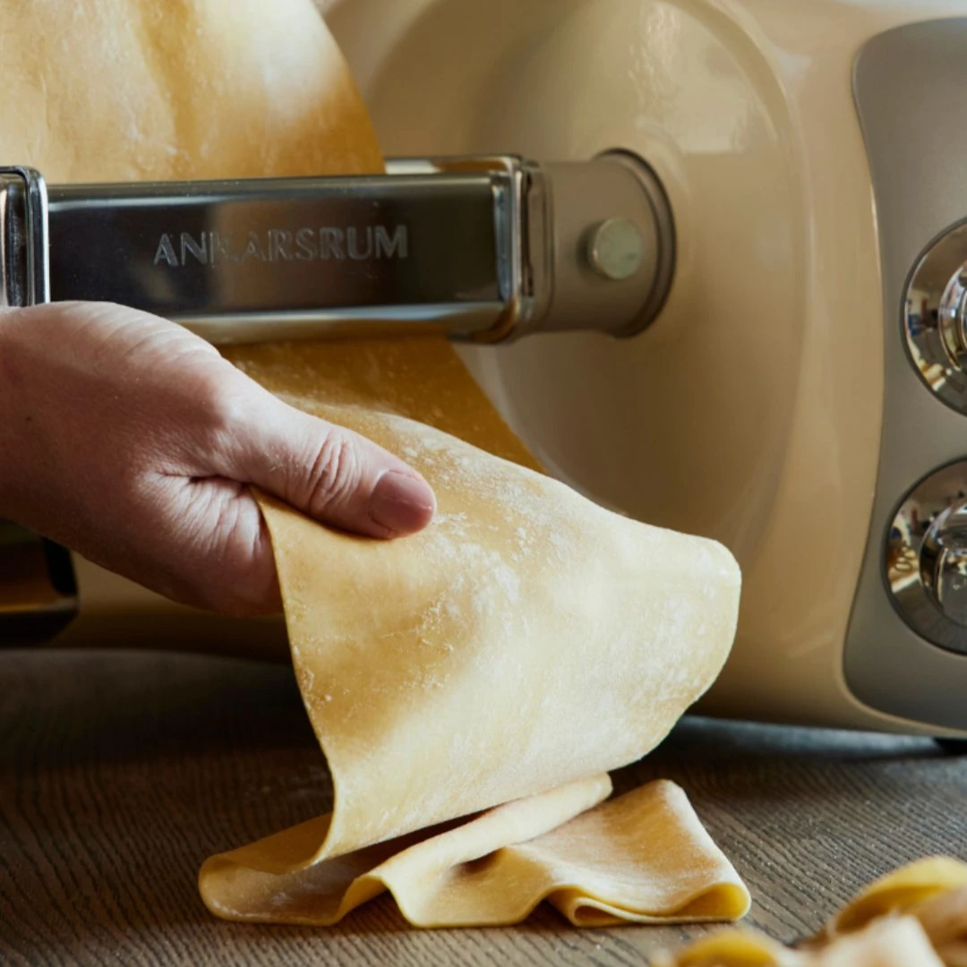 Tunn, jämn lasagneplatta matas ut genom Ankarsrums pastavalsar medan en hand tar emot degen.