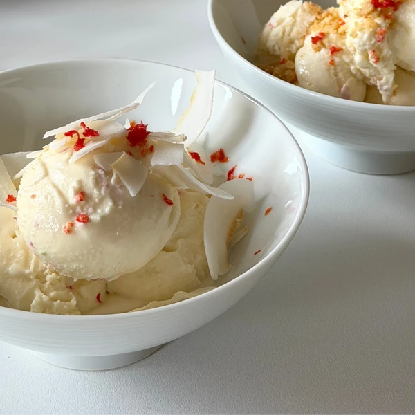 Creamy homemade ice cream scoops topped with coconut flakes and red berry crumbles served in white bowls.