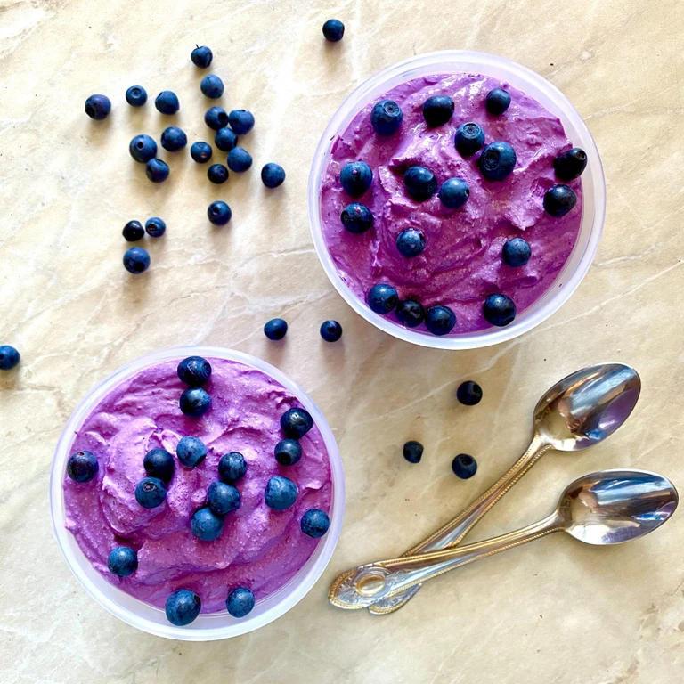 Two bowls of creamy blueberry mousse topped with fresh blueberries, made with an Ankarsrum stand mixer, beside vintage spoons.