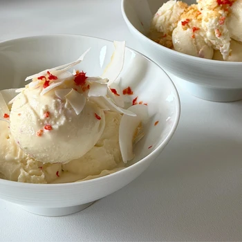 Creamy homemade coconut ice cream scoops topped with coconut flakes and red berry crumbles served in white bowls.