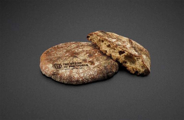 Rustic sourdough flatbread stamped with The Bread of the World – Ankarsrum logo, one whole and one broken piece showing airy crumb.