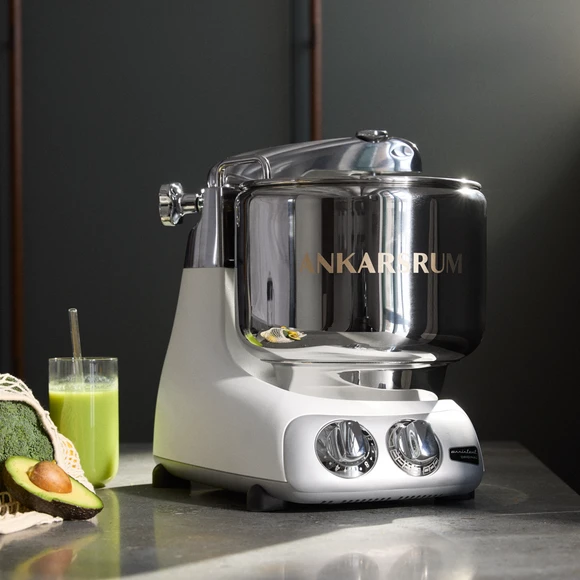 Close-up of the Ankarsrum Assistent Original in Mineral White, with a glass of green juice, broccoli and an avocado beside it.