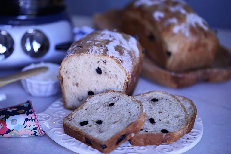 Freshly baked raisin bread loaf with sliced pieces on a white plate, made using an Ankarsrum stand mixer in the background.
