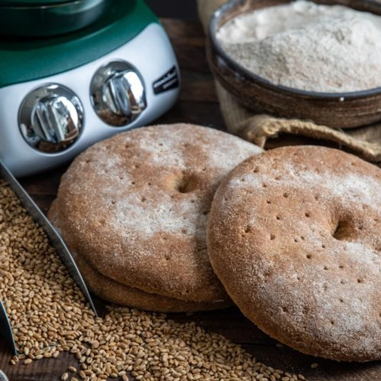 Whole grain bagels made with Ankarsrum stand mixer, surrounded by wheat berries and flour, showcasing homemade bread baking.