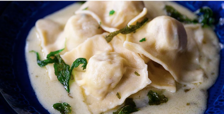 Homemade tortellini pasta in creamy white sauce with fresh herbs, made with Ankarsrum stand mixer pasta attachment.