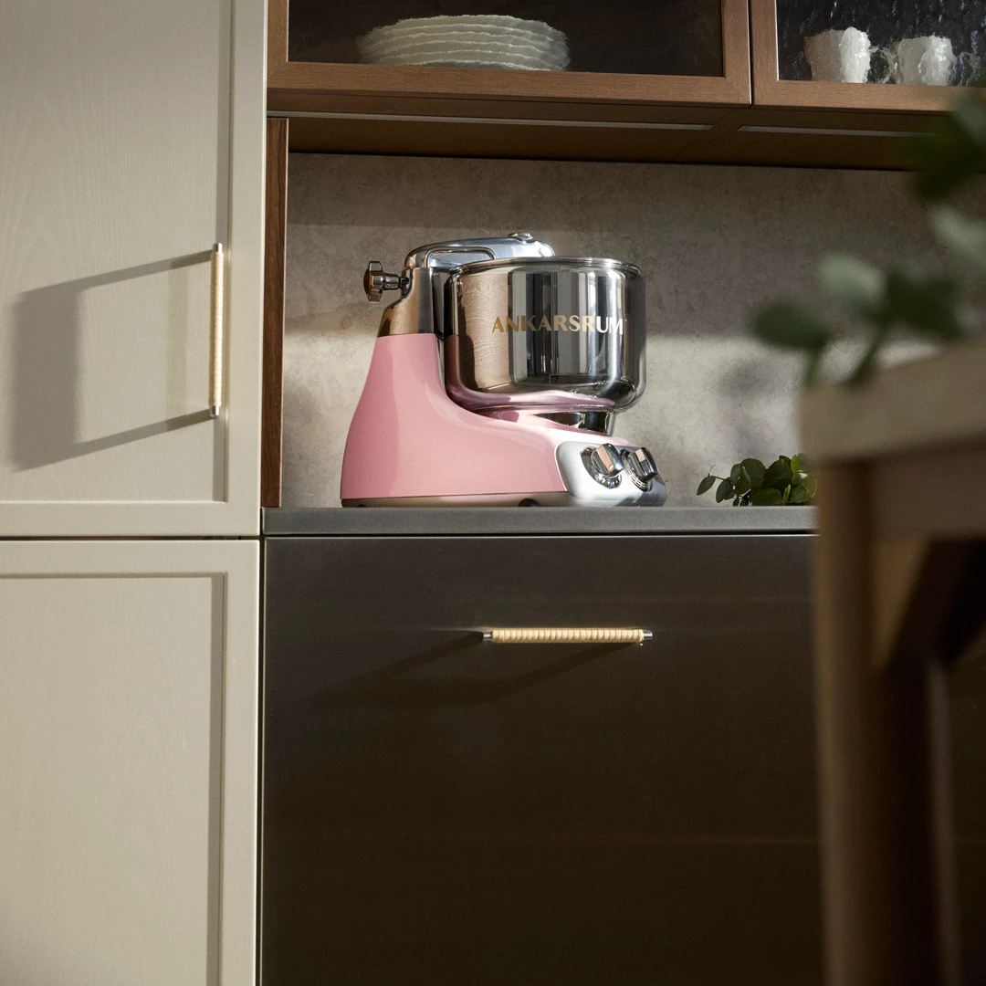 An Ankarsrum Assistent Original in Cloudy Pink on a kitchen countertop, surrounded by warm natural light.