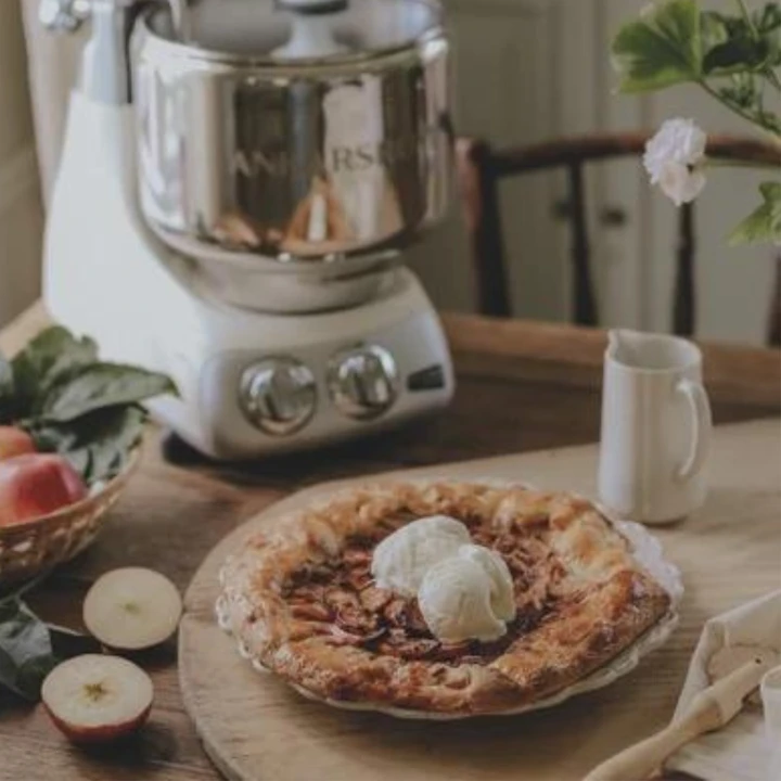 A delicious apple galette on a wooden cutting board with an Ankarsrum kitchen assistant in the background.