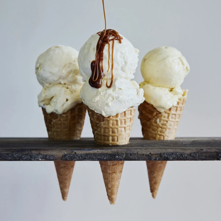 Three vanilla ice cream waffle cones on a wooden rack, center cone drizzled with caramel sauce, made with Ankarsrum.