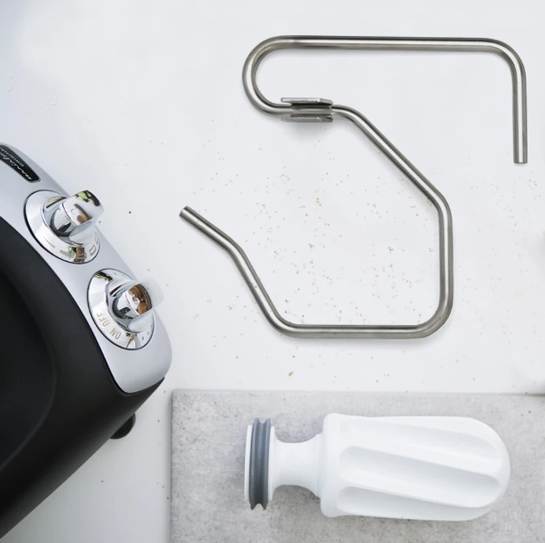 Ankarsrum stand mixer with stainless steel dough hooks and white roller attachment displayed on a white surface.